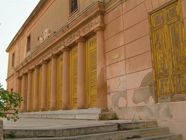 Pink facade with weathered yellow shutters and columns, peeling plaster, stone steps