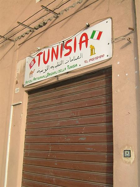 White Tunisia sign above a closed brown shutter on a pink wall