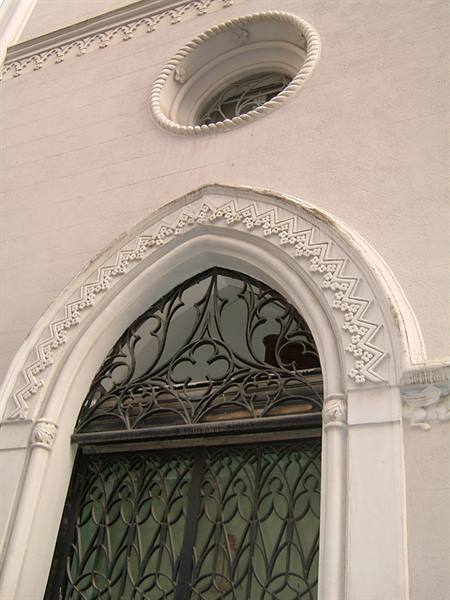 White facade with gothic arch, decorative black iron grille and round oculus