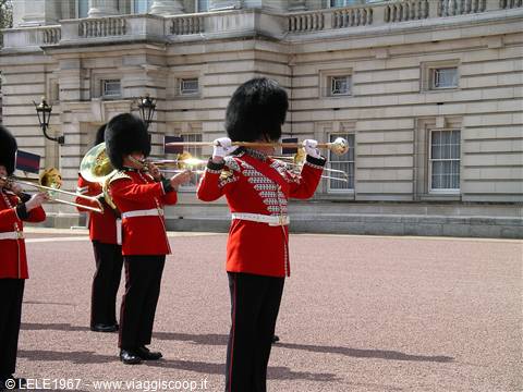 Guards in red tunics and bearskins play trombones outside Buckingham Palace