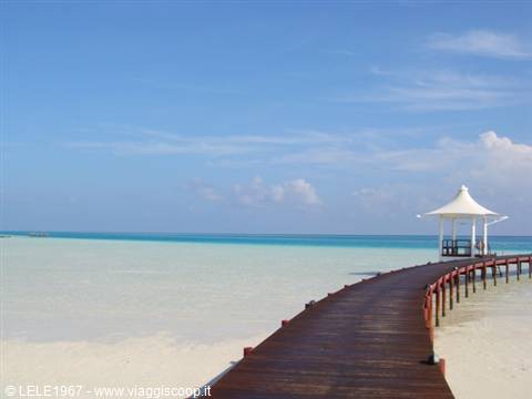 Wooden pier over turquoise water leading to a white gazebo, clear sky