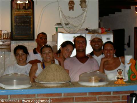 Smiling young group behind a brick counter with cakes under glass domes
