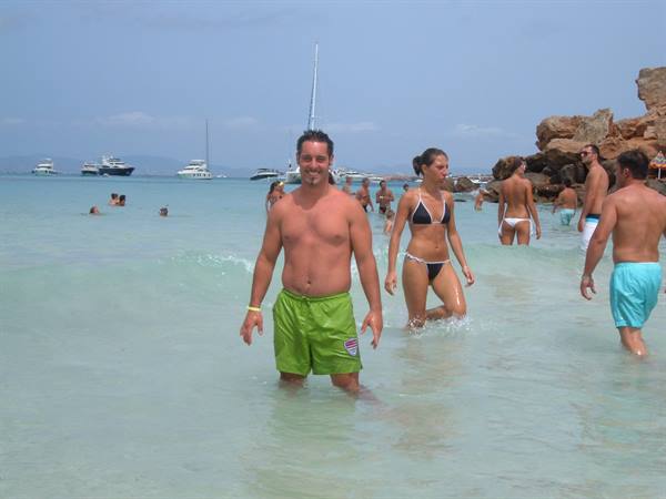 Swimmers in turquoise water with yachts and rocks, busy sea