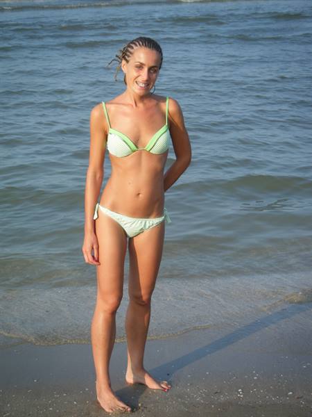 Smiling woman in a green bikini standing at the shoreline, water behind her