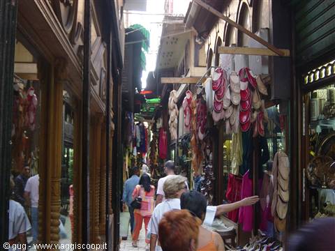 Covered bazaar with hanging slippers and tourists among wooden shops