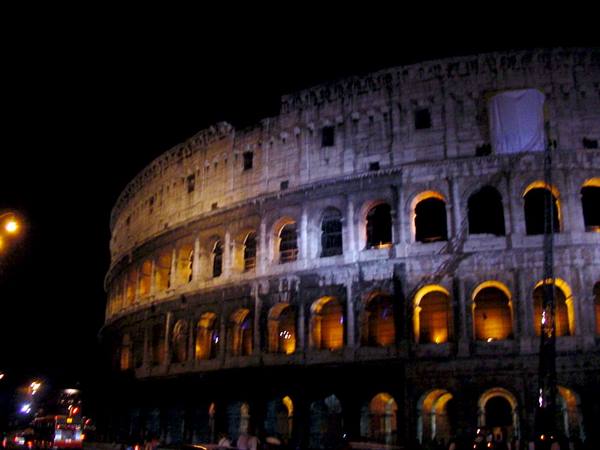 The Colosseum at night, travertine arches lit up, traffic below