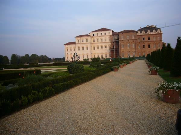 Gravel path through Venaria Reale gardens, flower pots and lit palace facade