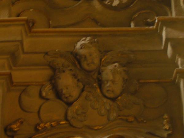 Three carved cherub heads on gilded baroque woodwork, warm church light