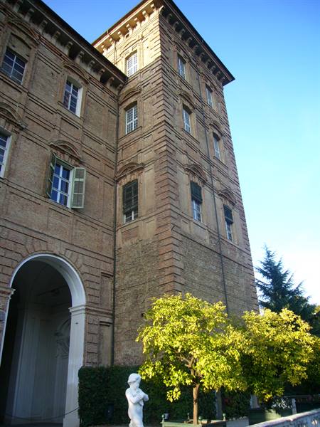 Brick tower of the Ducal Palace in Modena, morning sun, statue and citrus trees