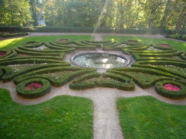 Central fountain in formal garden, geometric boxwood hedges with red flowers