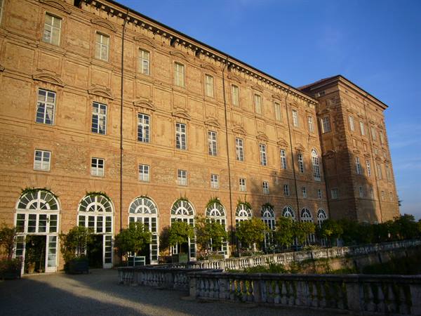 Brick facade of Venaria Royal Palace with arched windows and potted citrus trees