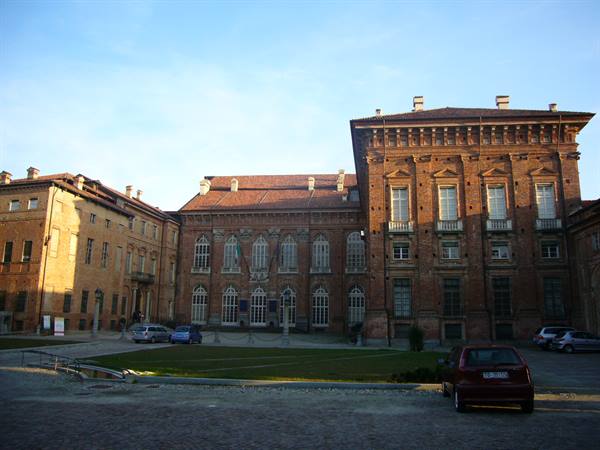Racconigi Castle, brick facade in sunlight, cars parked on the square