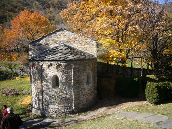 Stone Romanesque chapel with apse among autumn trees, two visitors