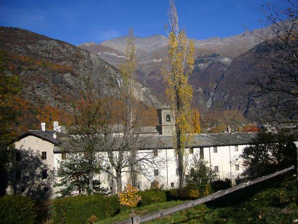 Monastery with bell tower among autumn trees and mountains, Aosta