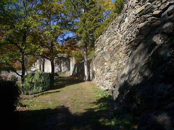 Grassy path between dry-stone walls and autumn trees, old buildings ahead