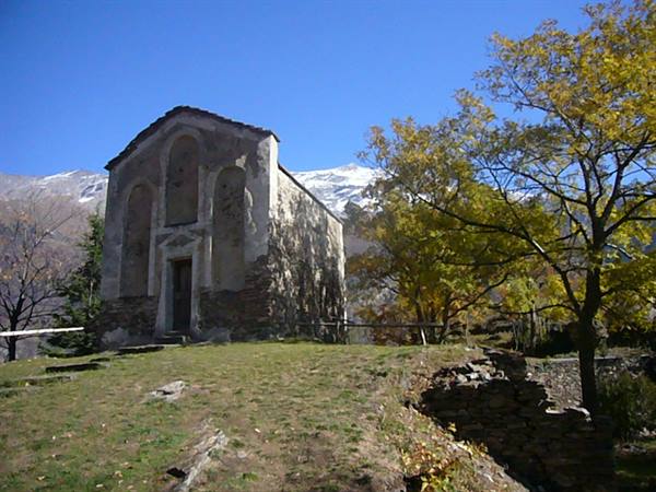 Ancient stone church among autumn trees, snow-capped mountains behind, blue sky