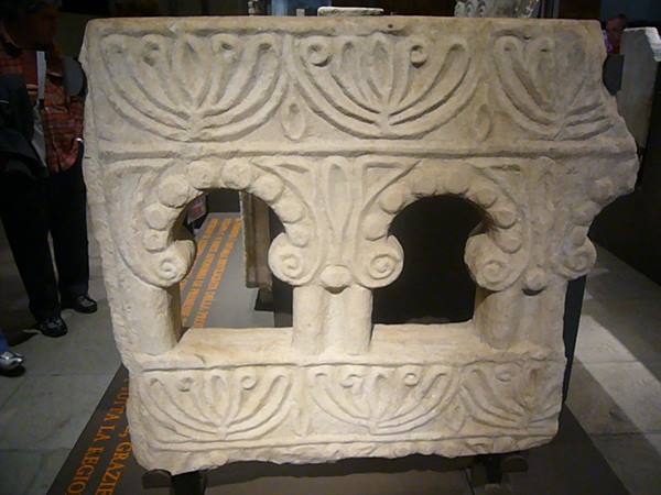 Carved stone slab with arches and palm motifs, displayed in a museum