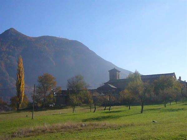 stone bell tower among autumn trees, green meadow beneath the mountain