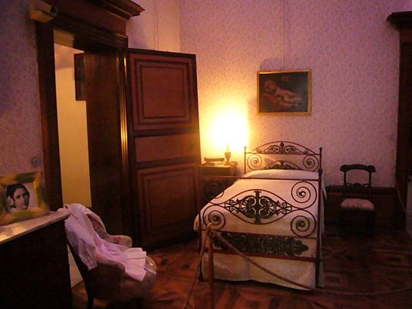 Vintage bedroom with wrought iron bed, lit lamp and framed painting on wallpaper