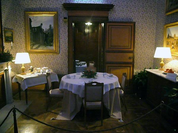 Dining room with set round table, lit lamps and gilded paintings on walls
