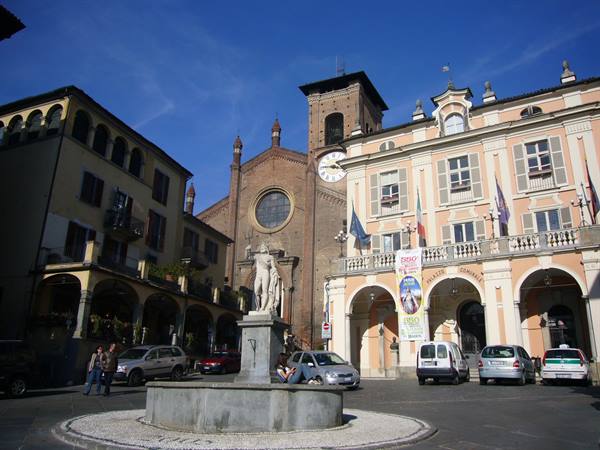 Fountain with statue in front of brick cathedral and ochre palace in Cesena