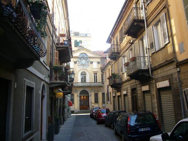 Cobbled alley with parked cars and buildings with wrought-iron balconies