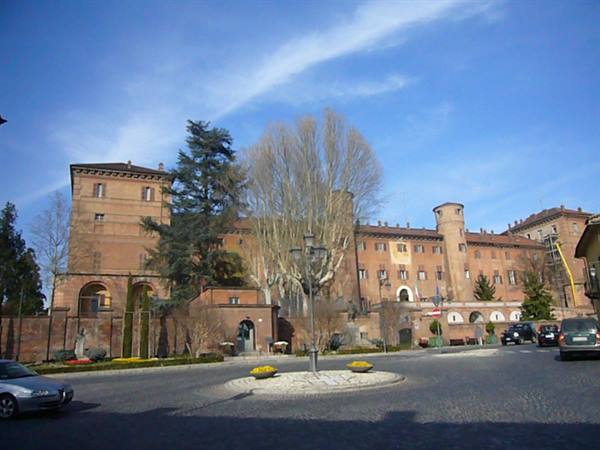 Red brick castle with round towers and cobbled square under blue sky