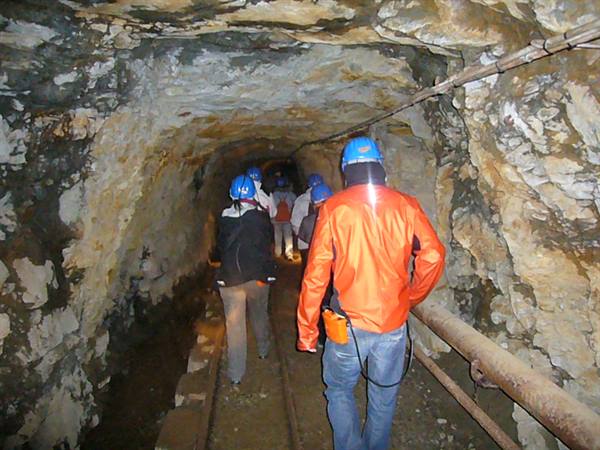 Visitors in blue helmets walk through a rock-hewn mine tunnel