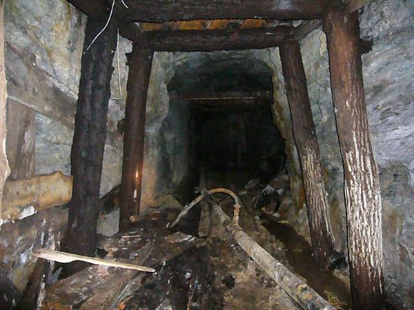 Abandoned mine tunnel with wooden beams and rusted rails
