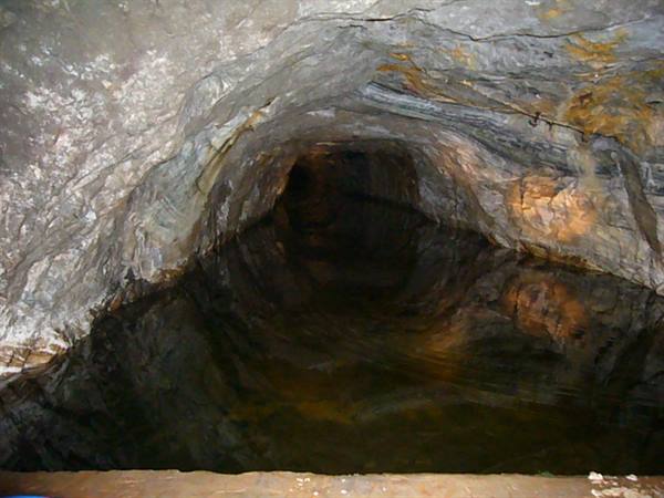 Rock-hewn tunnel with dark water, artificial lights on wet walls