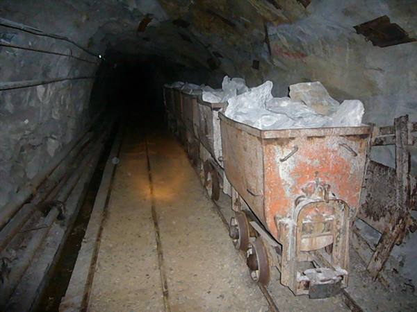 Rusty ore carts loaded with white mineral inside a dark mine tunnel