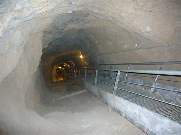 Tunnel carved into rock with metal walkway and sparse lights