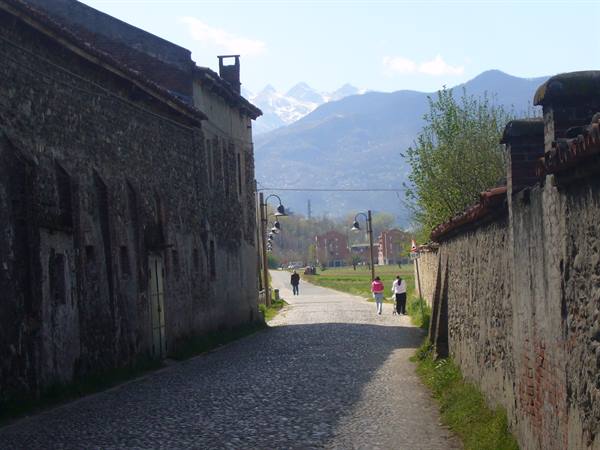 Cobblestone lane between stone walls, people walking, snowy mountains behind