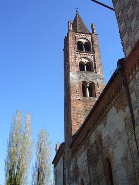 Romanesque brick bell tower with arched windows against blue sky, poplars nearby