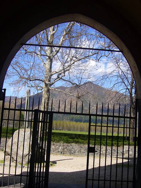 Iron gate beneath a stone arch, trees and mountain in the background