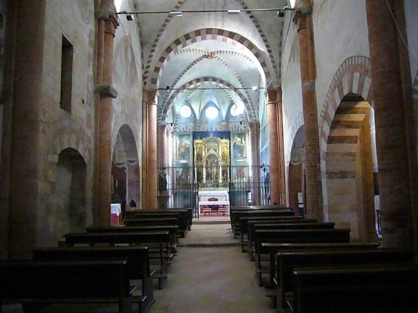 Romanesque church interior with brick columns, wooden pews and altar painting