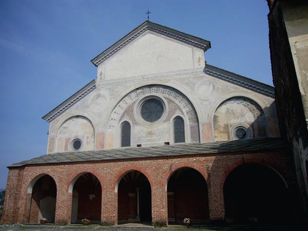Romanesque facade with rose window and arches, brick portico under blue sky