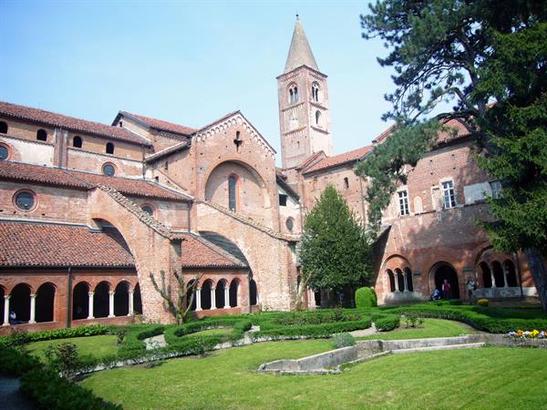 Brick cloister and Romanesque bell tower of Aquileia basilica, green garden
