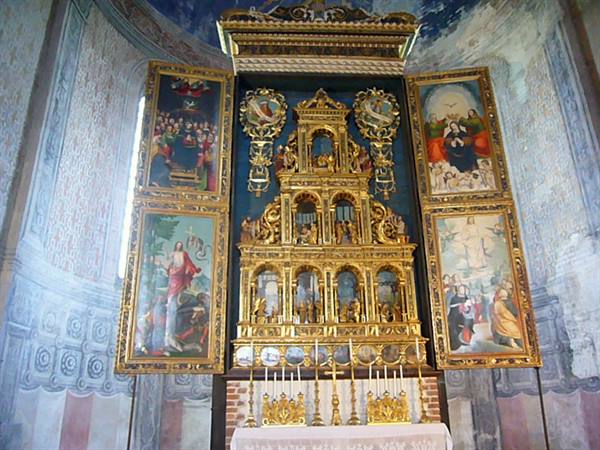 Ornate gilded altarpiece with painted panels inside a frescoed church