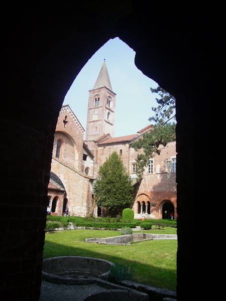 Brick cloister with Romanesque bell tower seen through a dark arch