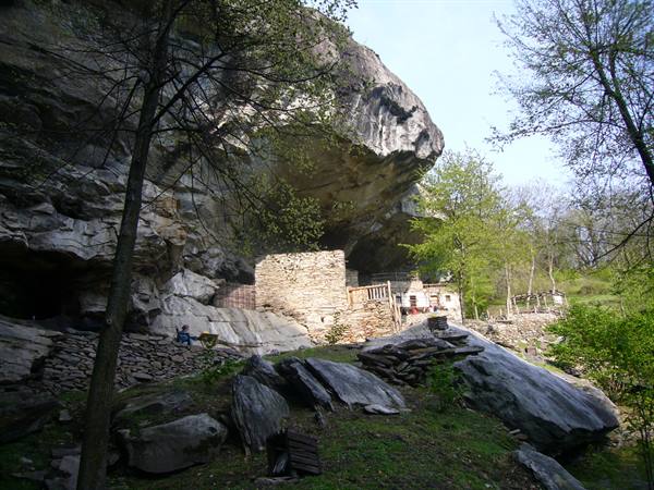 Stone houses sheltered beneath a huge boulder among green trees