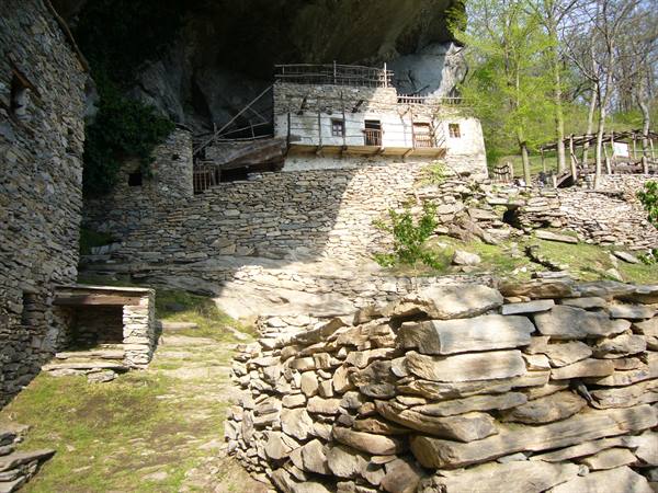 Old stone houses built beneath a large cliff, dry stone walls