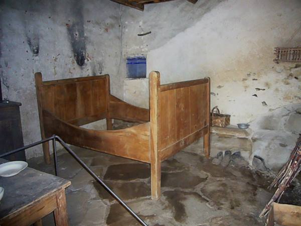 Old wooden bed in a rustic room with plastered walls and stone floor