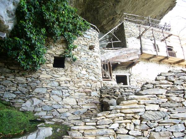 Dry-stone houses under a rock overhang, stone steps, green ivy