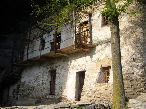 Whitewashed stone facade with wooden balconies, sunlight filtering through trees