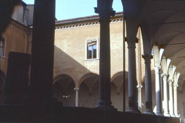 Stone columns and arches of a cloister, sunlight on ochre facade