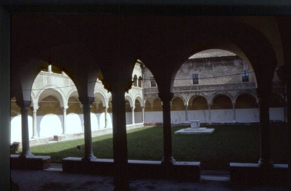 Cloister with Romanesque arches and a well in the grassy courtyard