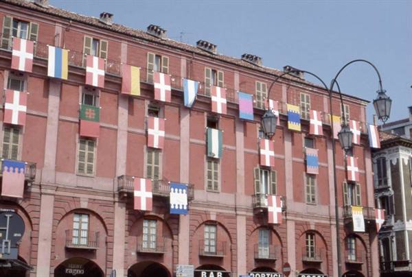 Red arcaded building with Savoy flags in Turin, wrought-iron street lamps