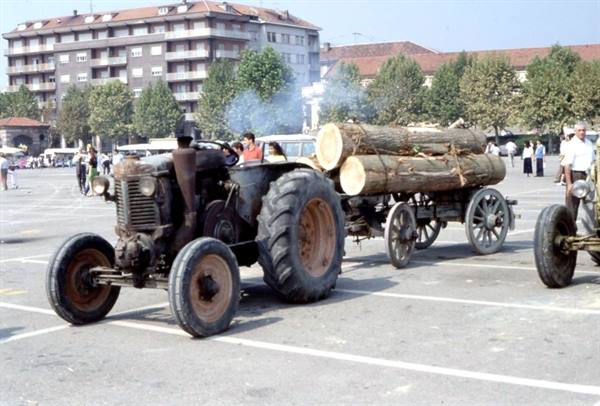 Old vintage tractor hauling logs across a busy town square