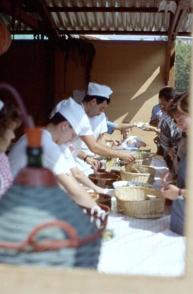 Cooks in white hats serve food from wicker baskets under a canopy